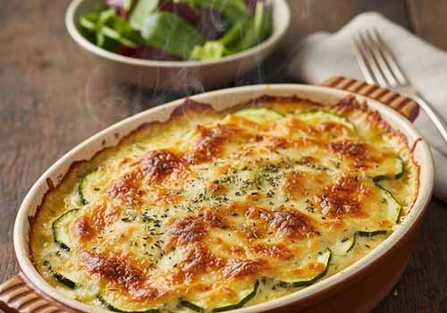 Gratin de courgettes sortant du four accompagné d'une salade dans un bol