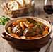 Ragout d'Agneau aux Légumes Racines et Romarin servi avec un verre de vin rouge et du pain