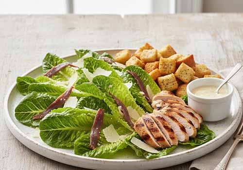 Salade César Déstructurée servie dans une assiette blanche avec la sauce César dans un petit pot à part