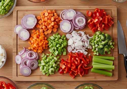 un plan de travail avec une planche à découper recouverte de différentes sortent de légumes émincés ainsi qu'un couteau de cuisine posé à côté 